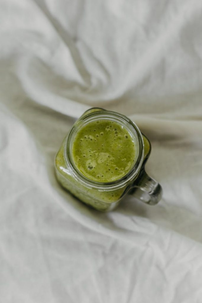green-and-white-ceramic-mug-on-white-textile-5644868 Top view of a nutritious green smoothie in a glass jar on a soft fabric background.